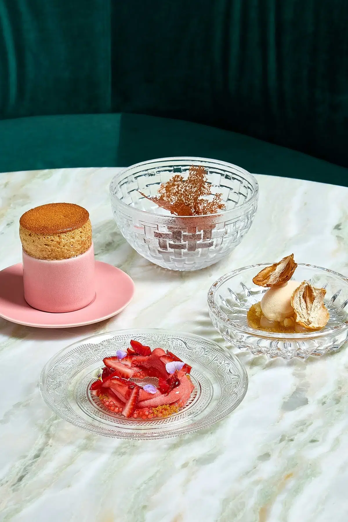 The four desserts are perfectly arranged on small plates and placed on the marble-patterned table.