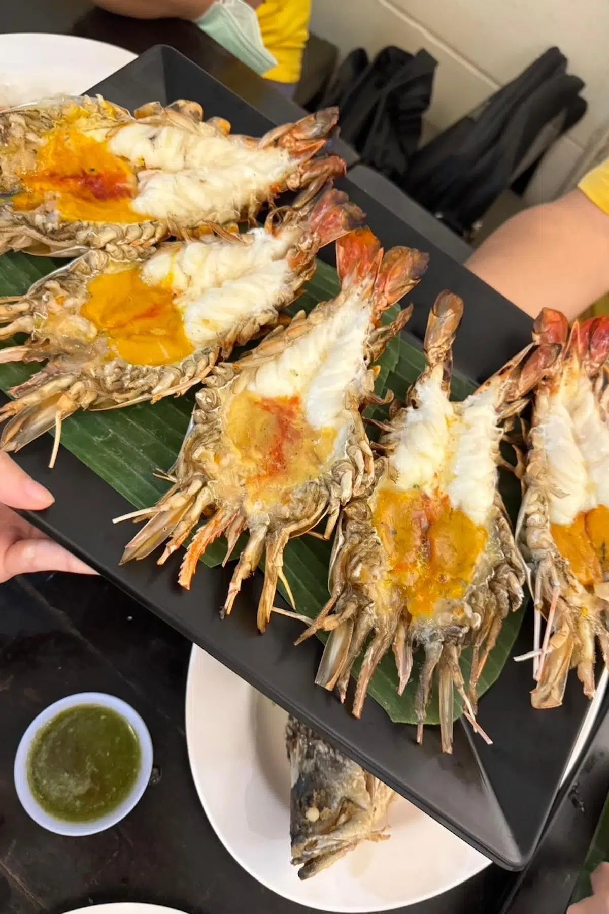 A Grilled river prawns with vibrant orange roe served on banana leaves, paired with green seafood dipping sauce. The dish highlights fresh and flavorful Thai seafood.