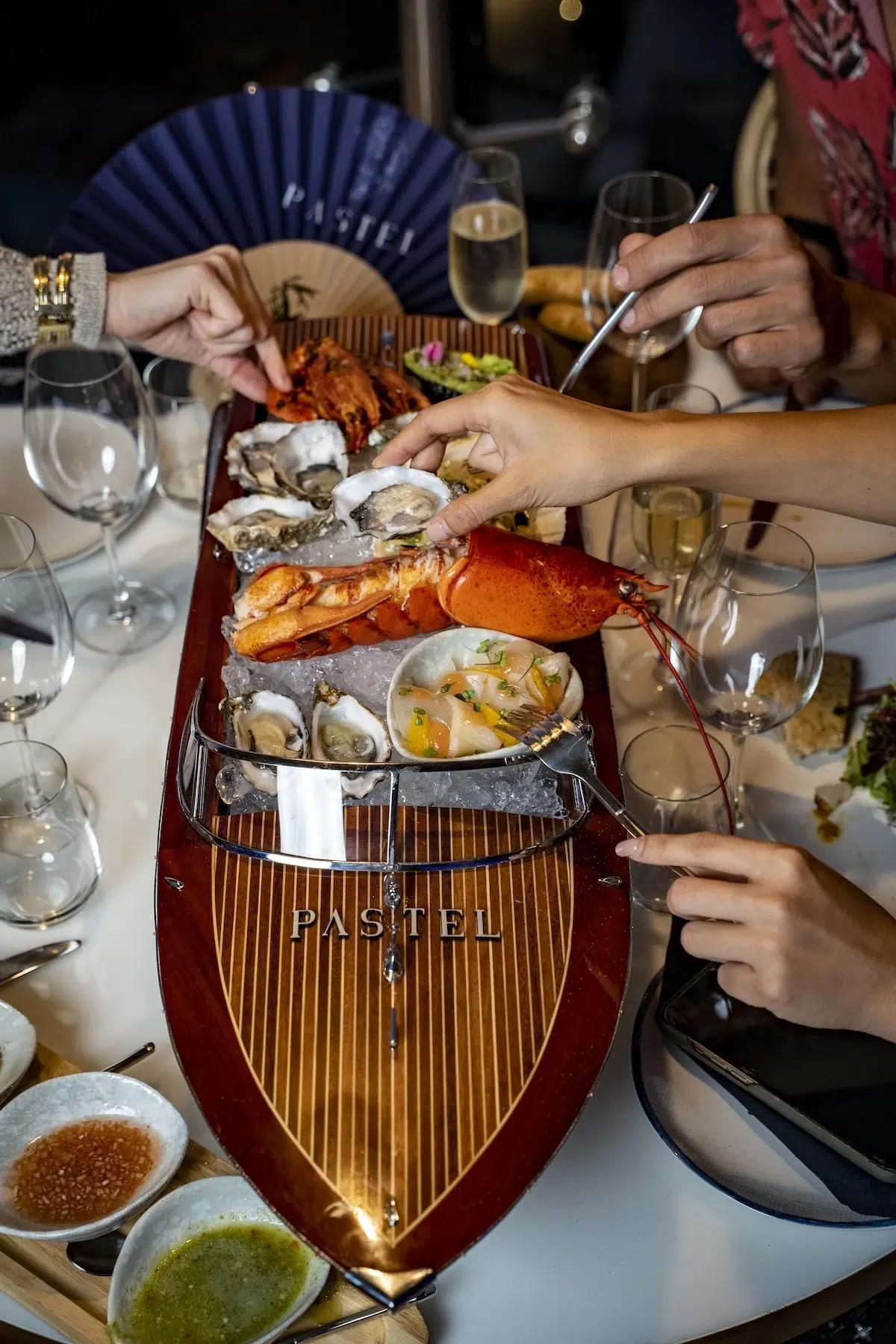 A hand is picking up an oyster with lobster on a yacht-shaped plate at Pastel Rooftop Bar.