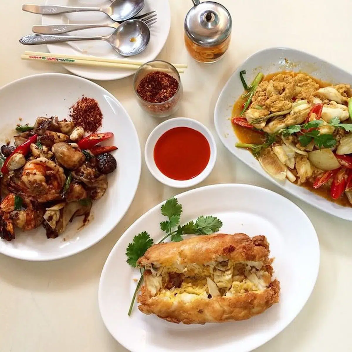 A Thai seafood restaurant called Jay Fai. On the left is a stir-fry with prawns, crab meat, and mushrooms. The top-right dish features crab meat in a yellow curry sauce. The bottom dish is a stuffed crab omelette, golden and crispy, served with a side of chili sauce.